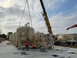 Workers guide the feet of an ion exchange vessel to its resting position while a crane operator slowly lowers it down. Workers guide the feet of an ion exchange vessel to its resting position while a crane operator slowly lowers it down.