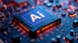 Orange light glows from the pins of a processing unit attached to a deep navy circuit board, the letters Ai shining brightly from the center of the processor.