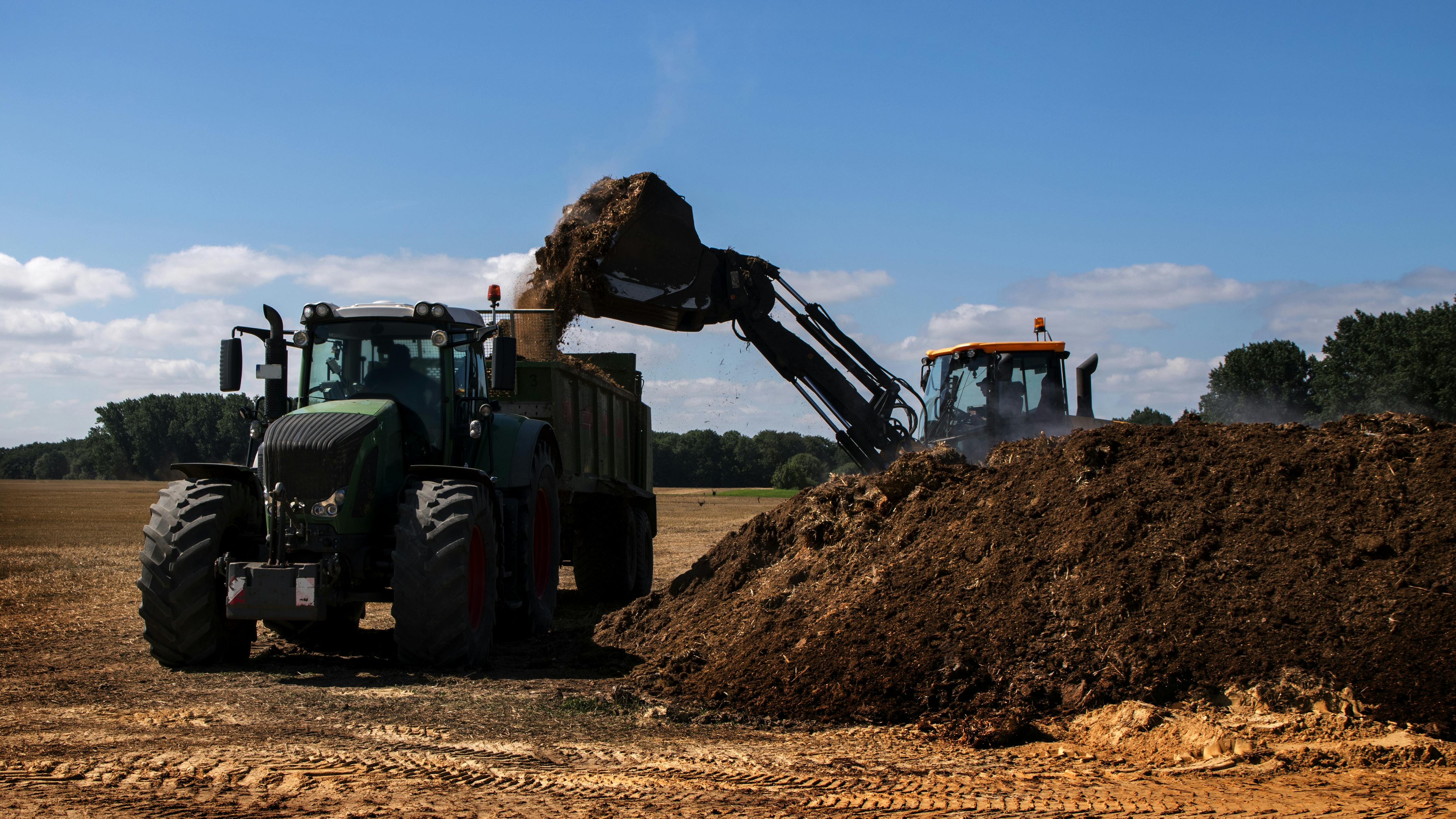Excavator loads tractor with fertilizer for farming. 57% of wastewater biosolids are land applied as fertilizer in the United States.